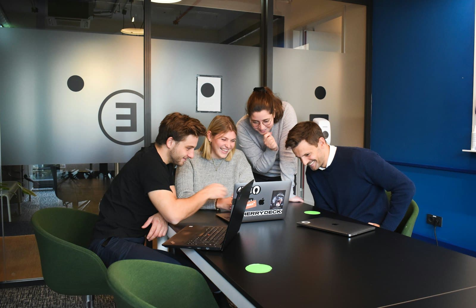 Four colleagues gathered around a laptop, smiling at something on the screen